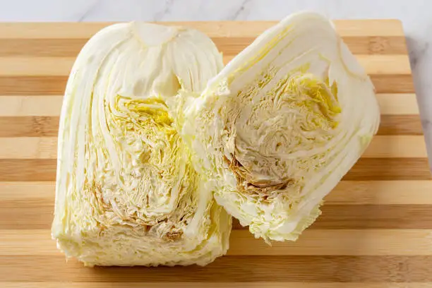 Rotten napa cabbage cut in half on a chopping board. The cabbagehead spoils from the inside. The rotting inside a chinese cabbage close-up. Food waste, spoiled vegetables concepts. Top view.