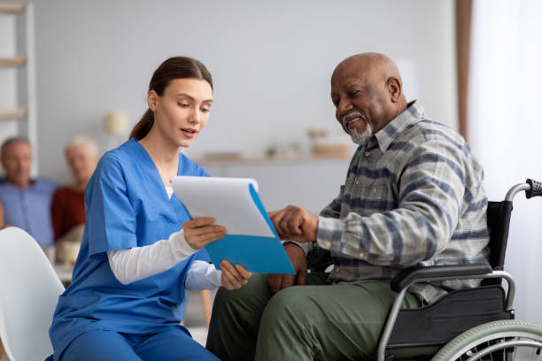 Attractive young nurse helping senior black man with questionnaire Attractive young woman in blue workwear nurse helping senior black man in wheelchair with questionnaire, african american pensioneer filling papers at nursing home, having assistance elder care stock pictures, royalty-free photos & images