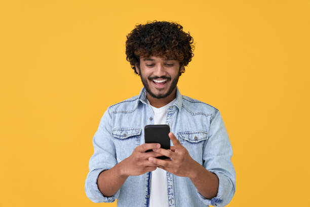 istock Happy indian young man using cell phone isolated on yellow background. 1368989994