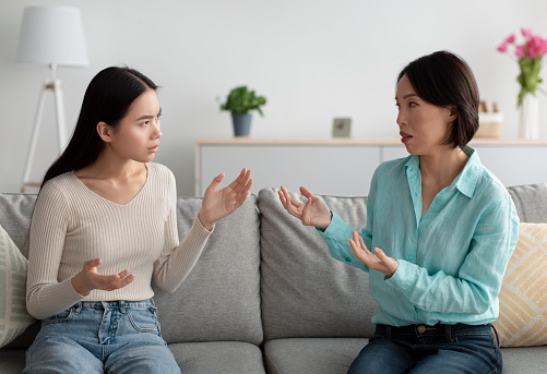 Infeliz mujer asiática madura y su hija adulta teniendo peleas, discutiendo entre sí en el sofá de la sala de estar photo