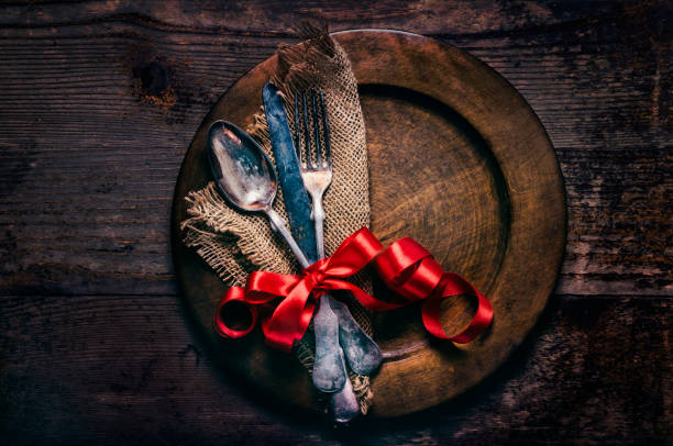 Valentines day dinner setting with vintage silverware, dinner plate and red ribbon on wooden table. Valentine day background frame for special romantic dining celebration. Top view.