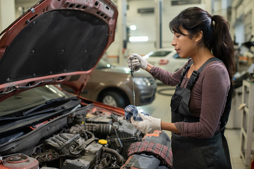 Side view portrait of young female mechanic checking oil levels while repairing car in workshop, copy space