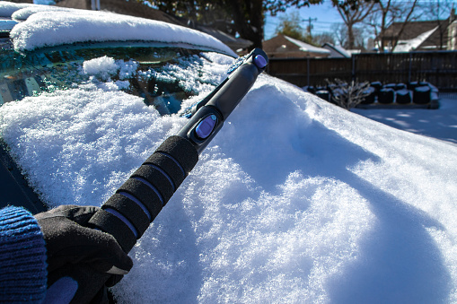 Scraping snow off of car windshield - hand in glove and telescoping ice scraper with shadows - selective focus.