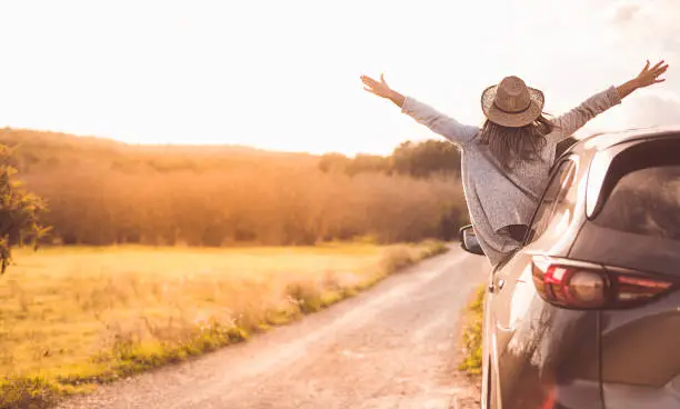 Photo of Happy girl celebrating success at sunset. The girl is wearing a hat and her arms are outstretched.
