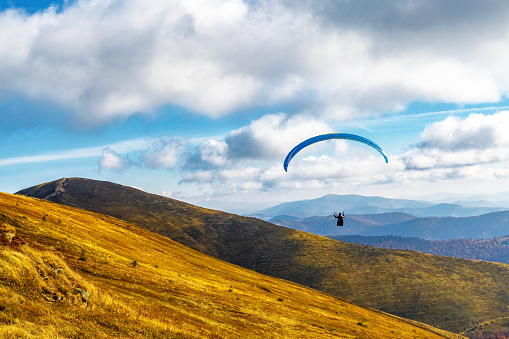 Tourist practices paragliding active sports in highland against giant forestry mountains illuminated by bright sunlight on sunny autumn day