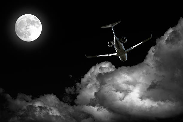 corporate jet airplane flying at night with full moon and storm clouds