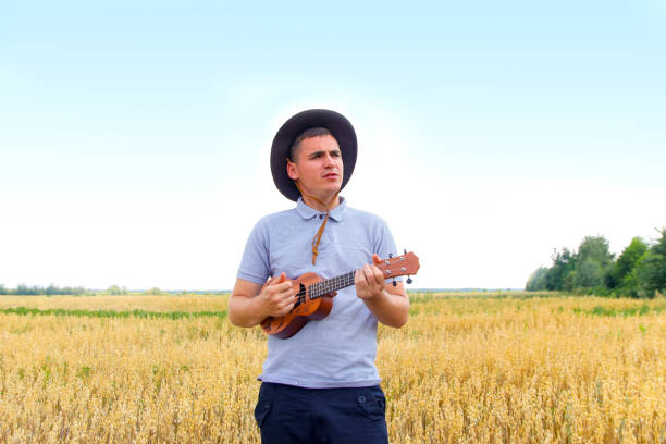 A man in a checkered shirt plays an acoustic guitar outdoors under a vibrant-colored canopy, creating a musical and lively atmosphere in bright daylight.