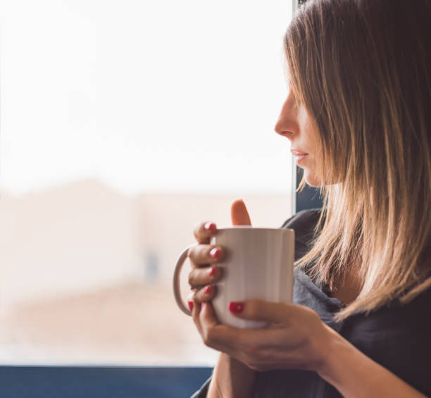 istock girl looking through a window while holding a white mug. She is in profile against the light. The light is golden and soft. Rest time. 1368999809