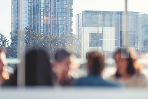 Defocussed image of Business people during a meeting with high rise buildings in the background. They are sitting in a board room, All are casually dressed.