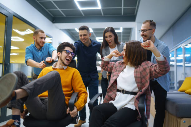 istock Young cheerful business people  having fun while racing on office chairs and smiling. 1369002486