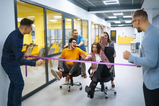 istock Young cheerful business people  having fun while racing on office chairs and smiling. 1369002527