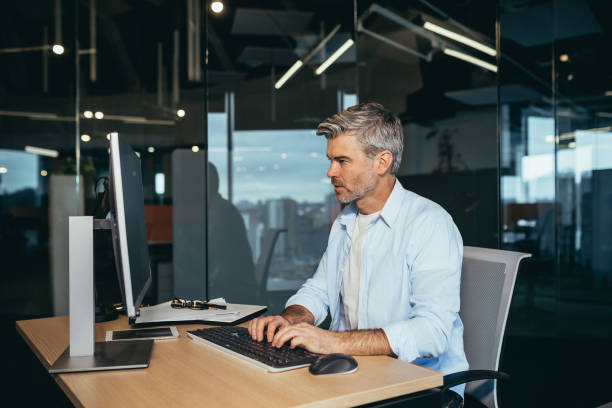 istock Experienced worker gray-haired businessman works at the computer in a modern office 1369002813