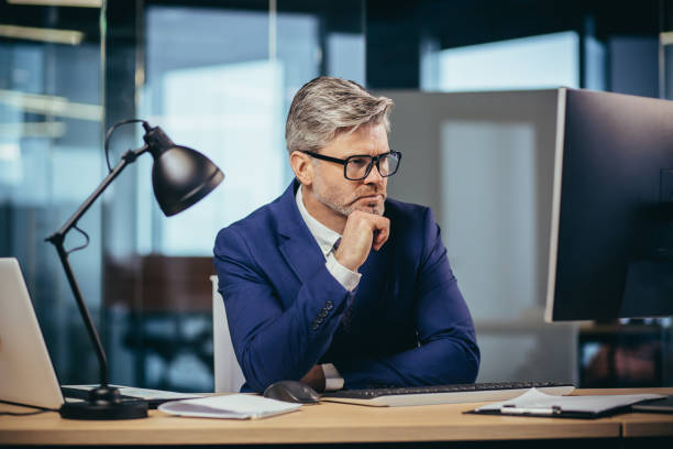 istock A gray-haired man with glasses thinks about the tasks, a businessman with a beard works in a modern office at the computer, 1369002871