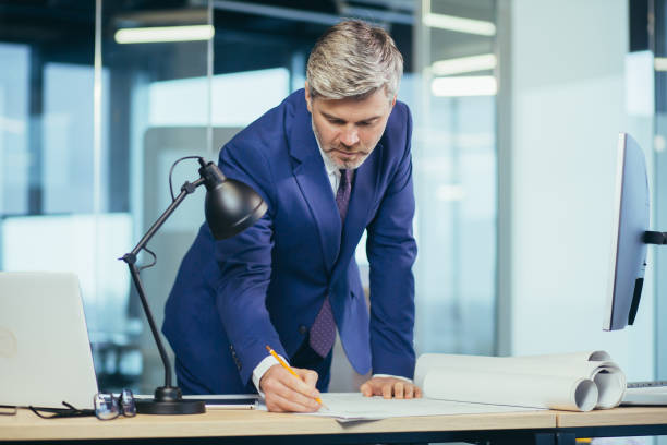 istock Experienced architect, working at the office desk on the drawing, makes final edits before handing over the object, a man in a modern office 1369002872