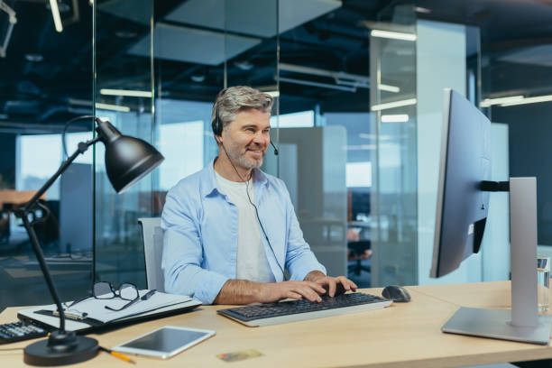 성공적인 사업가의 초상화, 회색 머리 남자는 비디오 통화에 동료에게 이야기, 헤드셋을 사용하여, 미소와 기뻐 - cyberspace support computer assistance 뉴스 사진 이미지
