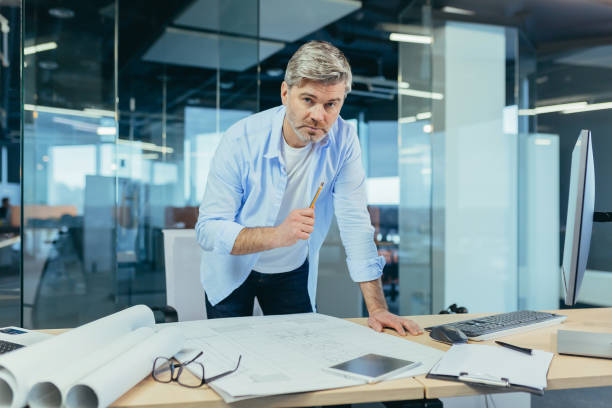 istock Experienced architect, working at the office desk on the drawing, makes final edits before handing over the object, a man in a modern office 1369002908