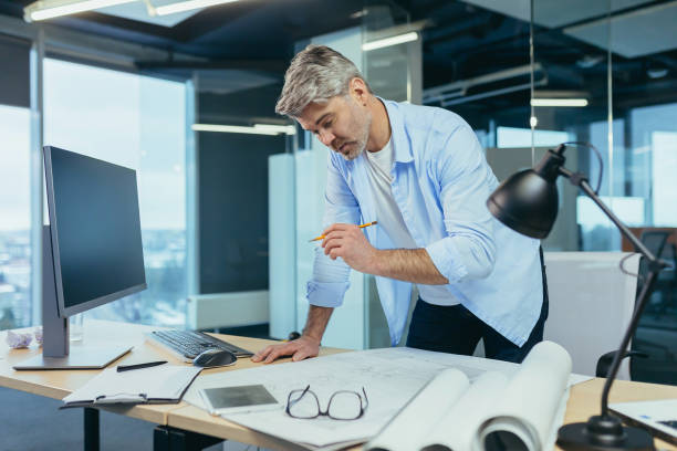 istock Experienced architect, working at the office desk on the drawing, makes final edits before handing over the object, a man in a modern office 1369002916