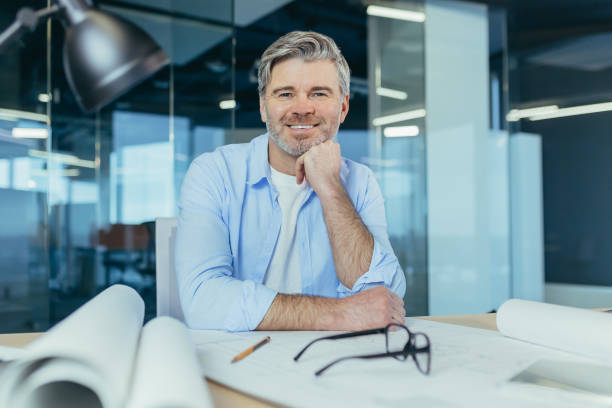 istock Experienced gray-haired designer architect, smiling and looking at camera, man working on architectural projector of new office center 1369002920