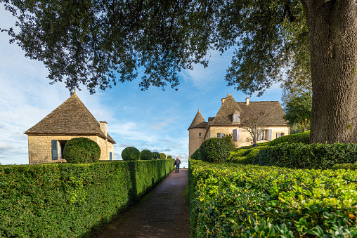 Vezac, France - October 31, 2021: Unrecognizable visitor walking up a path lined with clipped boxwood hedges in the garden of the Marqueyssac Castle in Perigord, taken on a sunny autumn afternoon