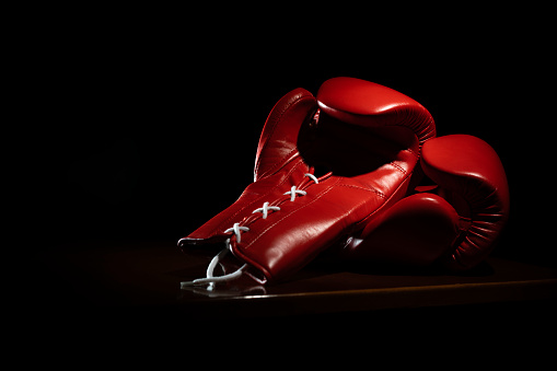 Shiny new red boxing gloves with laces in dim lighting on black background