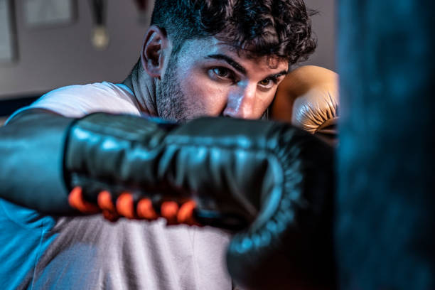 junger kaukasischer boxer schlägt mit boxhandschuhen auf die tasche - muay thai stock-fotos und bilder