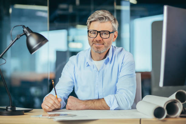 istock Experienced gray-haired designer architect, smiling and looking at camera, man working on architectural projector of new office center 1369005519