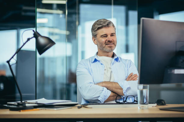 istock Experienced worker gray-haired businessman works at the computer in a modern office 1369006134