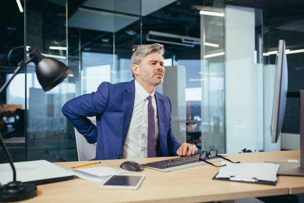 istock Tired worker businessman working in the office sitting at the computer, the man has severe back pain 1369007714