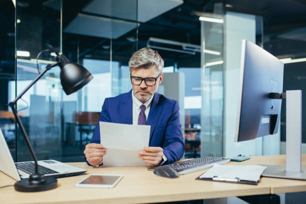 istock Experienced gray-haired businessman working at a computer, paperwork in the office, reading a letter from the bank 1369007895