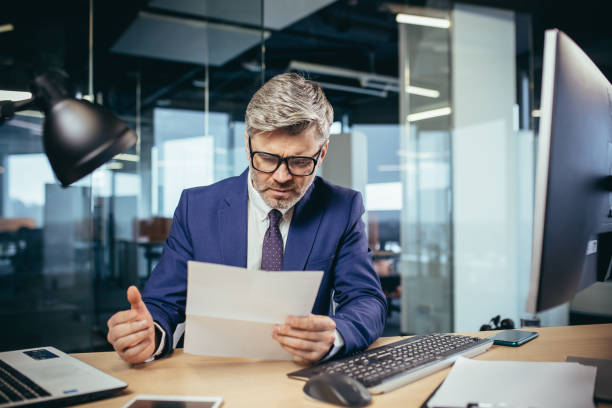 istock Experienced gray-haired businessman working at a computer, paperwork in the office, reading a letter from the bank 1369007896