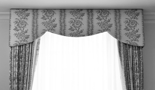 Black and white image of pelmet and brocade curtains with voile curtains. Copy space.