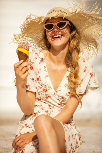 Gorgeous young woman sitting outdoors on stairs enjoying while eating ice cream at sunny day. She is tourist on vacation at Mediterranean islands and looks happy and carefree