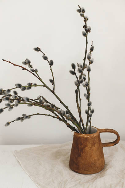 istock Willow branches in stylish rustic vase on wooden table. Modern Easter still life. Pussy willow branches in home, natural spring decor. Simple Easter rural minimal aesthetics. Space for text 1369009556