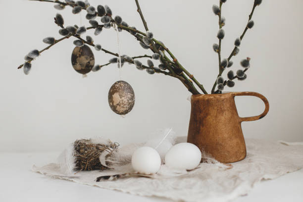 istock Easter rustic still life. Natural eggs, feathers, nest, willow branches in vase on aged wooden table. Simple stylish easter decoration on table aesthetics. Happy Easter 1369010229