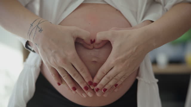 MS Couple connects their hands together in the shape of a heart around a pregnant belly