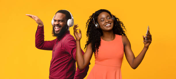 istock Positive black couple with wireless headsets having fun on yellow 1369010318