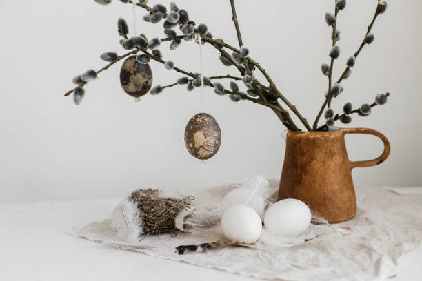 istock Easter rustic still life. Natural eggs, feathers, nest, willow branches in vase on aged wooden table. Simple stylish easter decoration on table aesthetics. Happy Easter 1369011611