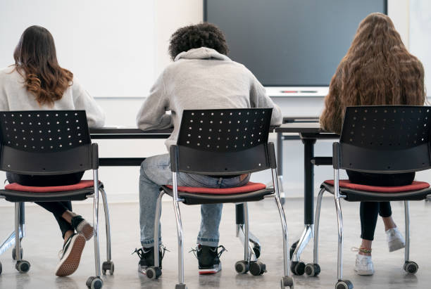 College Students in Class A small group of College students sit at their desks working away individually during class.  They are each dressed casually and can be seen from the back. middle eastern ethnicity mature adult book reading stock pictures, royalty-free photos & images