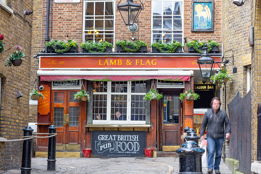 A man walks past the entrance to a commercial pub in London. Lamb & Flag dates from the early 18th century, having become a pub in at least 1772 (although back then it was called The Coopers Arms, changing to Lamb & Flag in 1833). In the upper area, bare-knuckle prize fights took place so the pub was nicknamed 'the bucket of blood'. The pub was often visited by writer Charles Dickens frequented the pub in the 1800s and was resurfaced with brick in 1958.