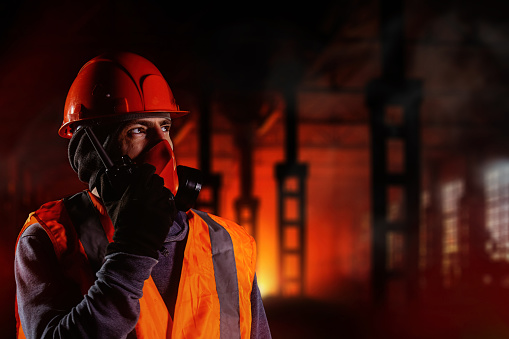 Man in respirator talking on walkie-talkie during fire in industrial building.