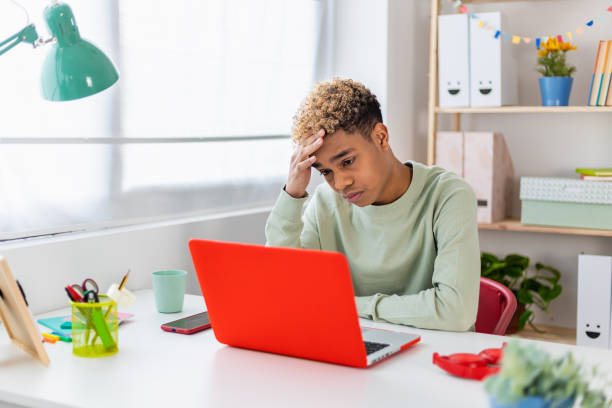 Portrait of stressed teenager boy sitting on desk in youth room stock photo