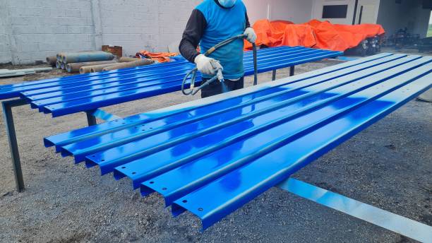 un pittore sta dipingendo una superficie d'acciaio blu per un edificio in acciaio - spray paint immagine foto e immagini stock