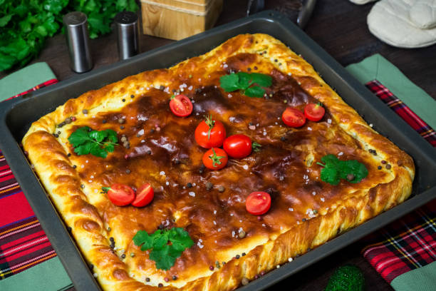 A square meat pie on an iron tray. Greased with butter, sprinkled with pepper and salt. Country style. Cooked at home. stock photo