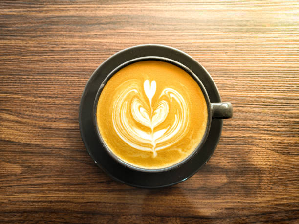 Beautiful hot coffee latte art design foam inside black cup with wooden background. Top view