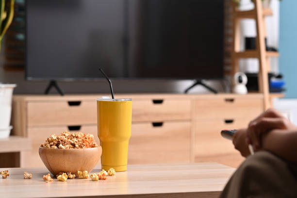 istock Young woman sitting on sofa with remote control while watching TV and eating popcorn. 1369066536
