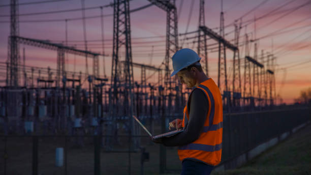confident male engineer using a laptop in front of electric power station - energiecentrale stockfoto's en -beelden