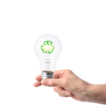 Close-up of hand holding a light bulb with recycling symbol against white background.\nConcept of clean energy and recycling.