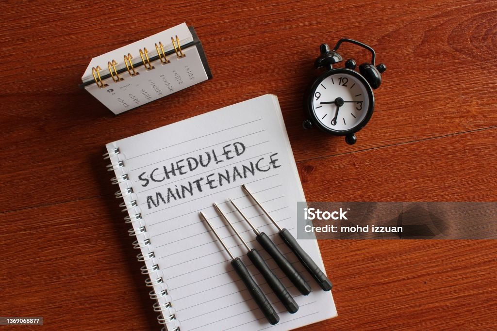 Calendar, alarm clock, screwdriver and book with text SCHEDULED MAINTENANCE. Top view image of calendar, alarm clock, screwdriver and book with text SCHEDULED MAINTENANCE. Repairing Stock Photo