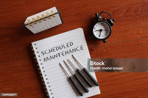 Calendar Alarm Clock Screwdriver And Book With Text Scheduled Maintenance Stock Photo - Download Image Now