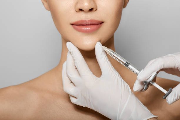 Syringe near woman's chin, beauty injections with fillers for chin shape correction. Cropped female face while procedure chin contouring Syringe near woman's chin, beauty injections with fillers for chin shape correction. Cropped female face while procedure chin contouring chin stock pictures, royalty-free photos & images